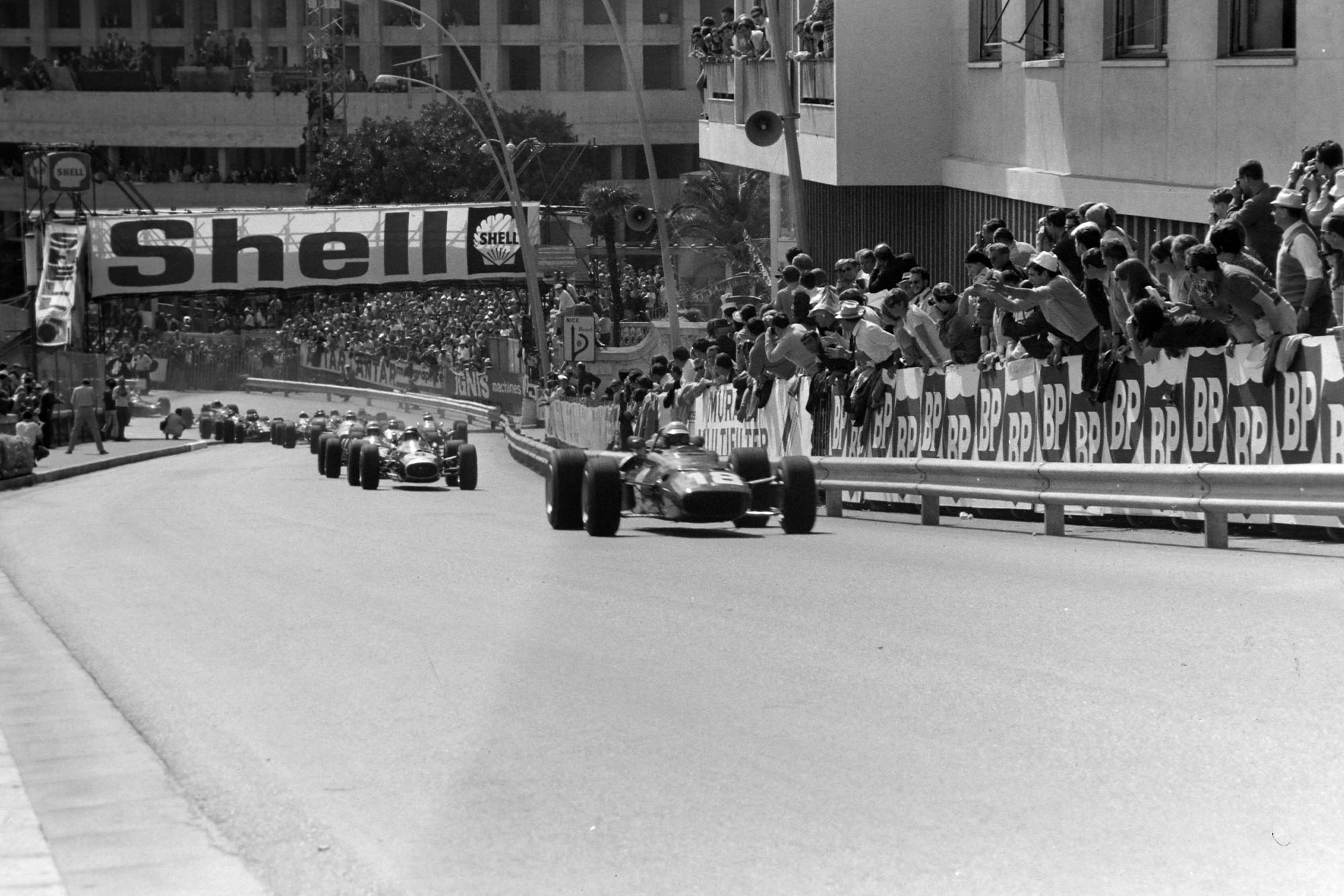 Lorenzo Bandini, Ferrari 312, leads Jack Brabham, Brabham BT19 Repco, and the rest of the field up Beau Rivage at the start.