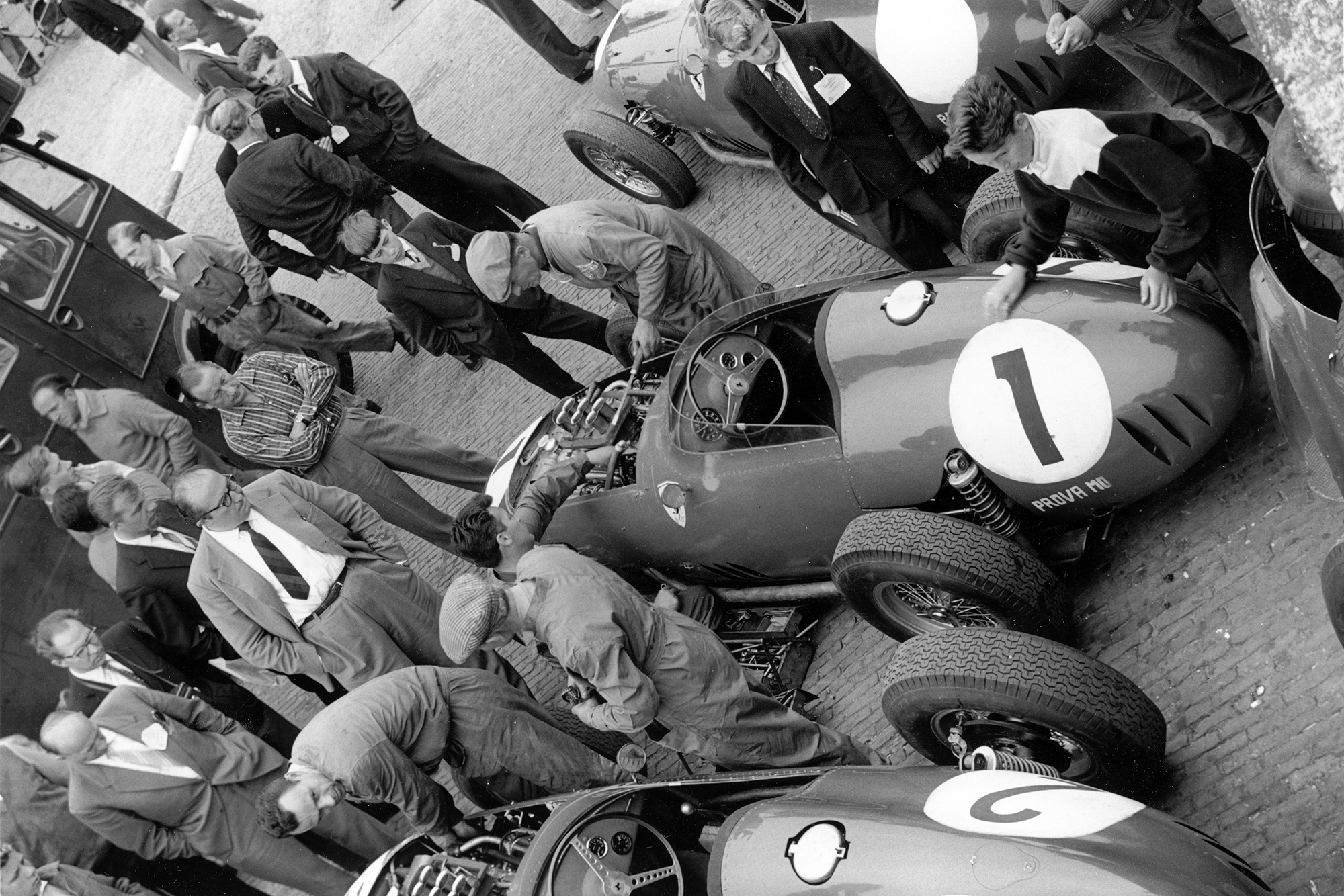 In the paddock Carlo Chiti (glasses, centre) overseas mechanics working on the Ferrari Dino 246 of Jean Behra.