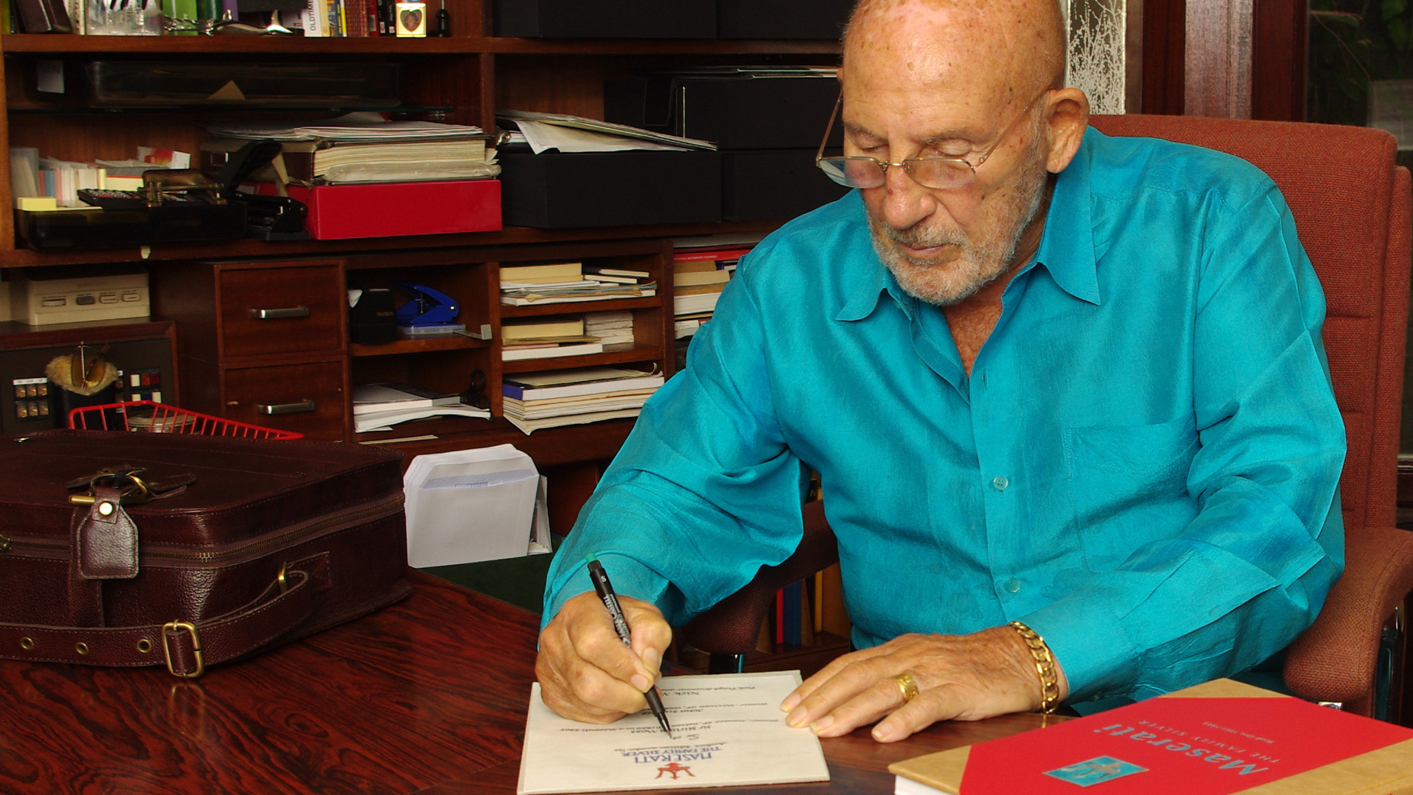 Stirling Moss signing a presentation page of Maserati The Family Silver book